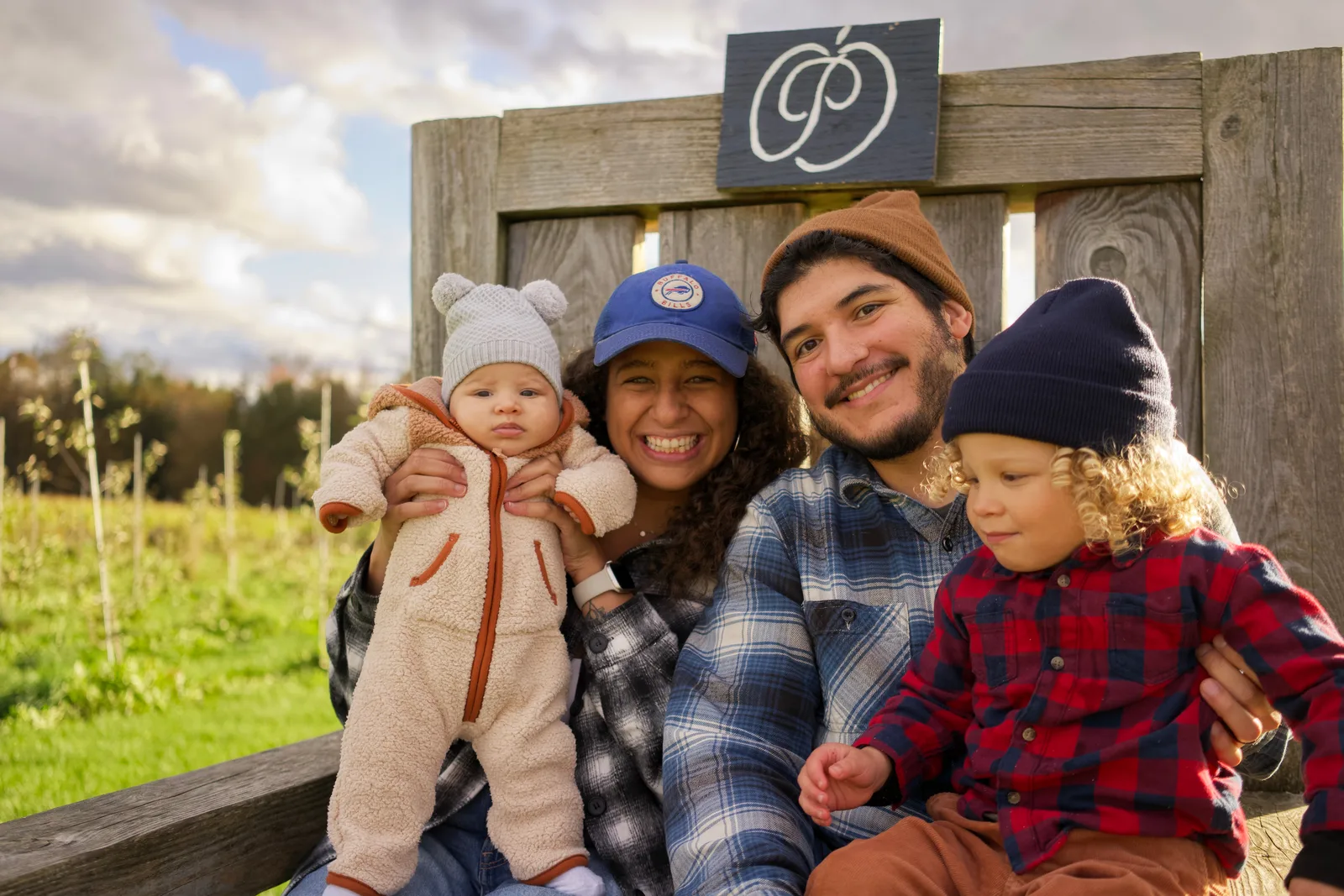 Four people on wooden bench, sign above, grassy field and forested hills in distance
