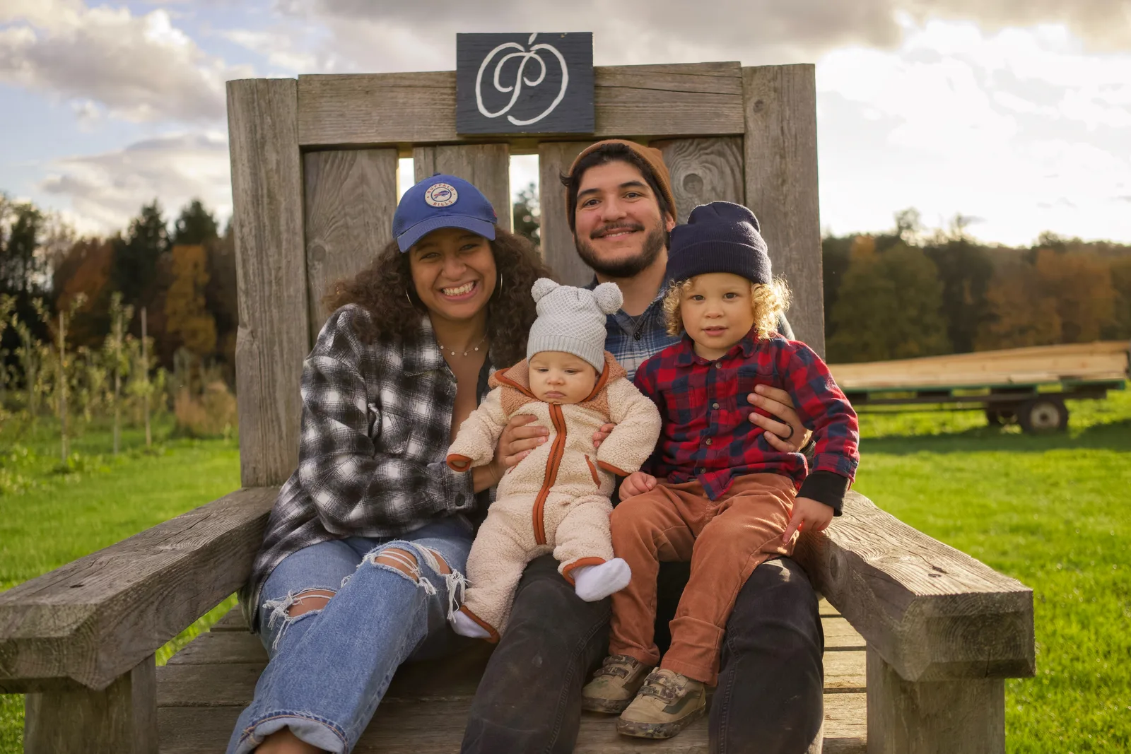 Four people on wooden bench, sign above, open field with distant trees and mountains