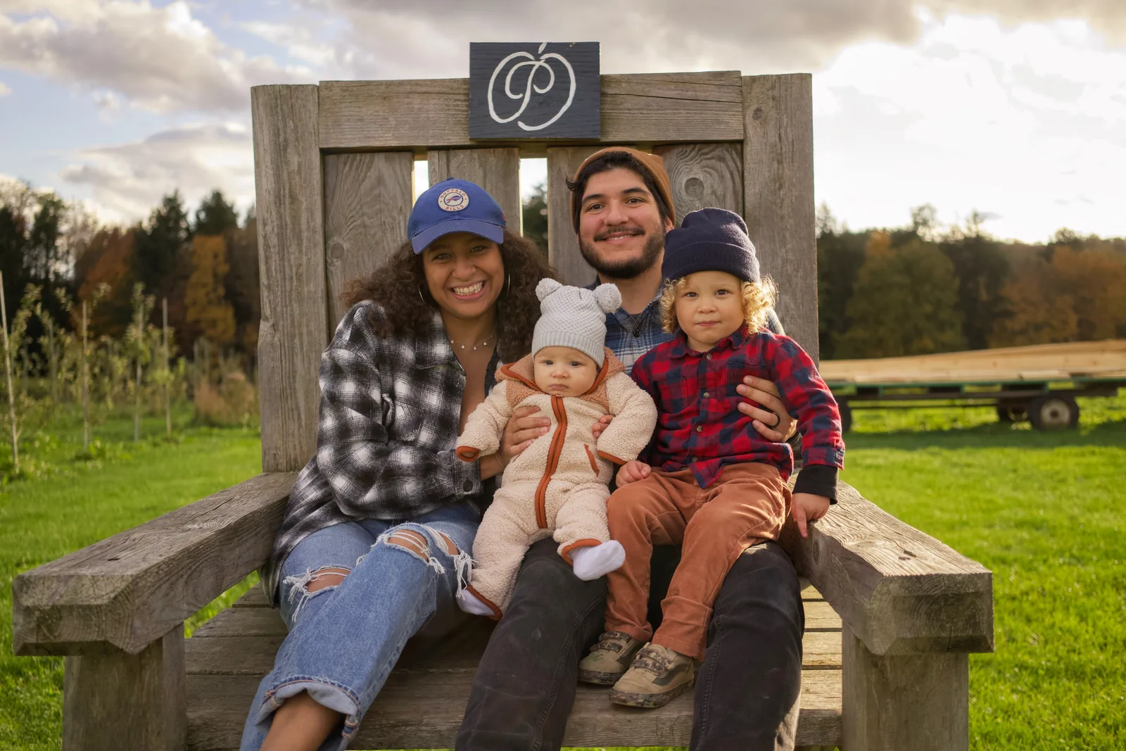 Four people on wooden bench, sign above, grassy field with farm equipment in background