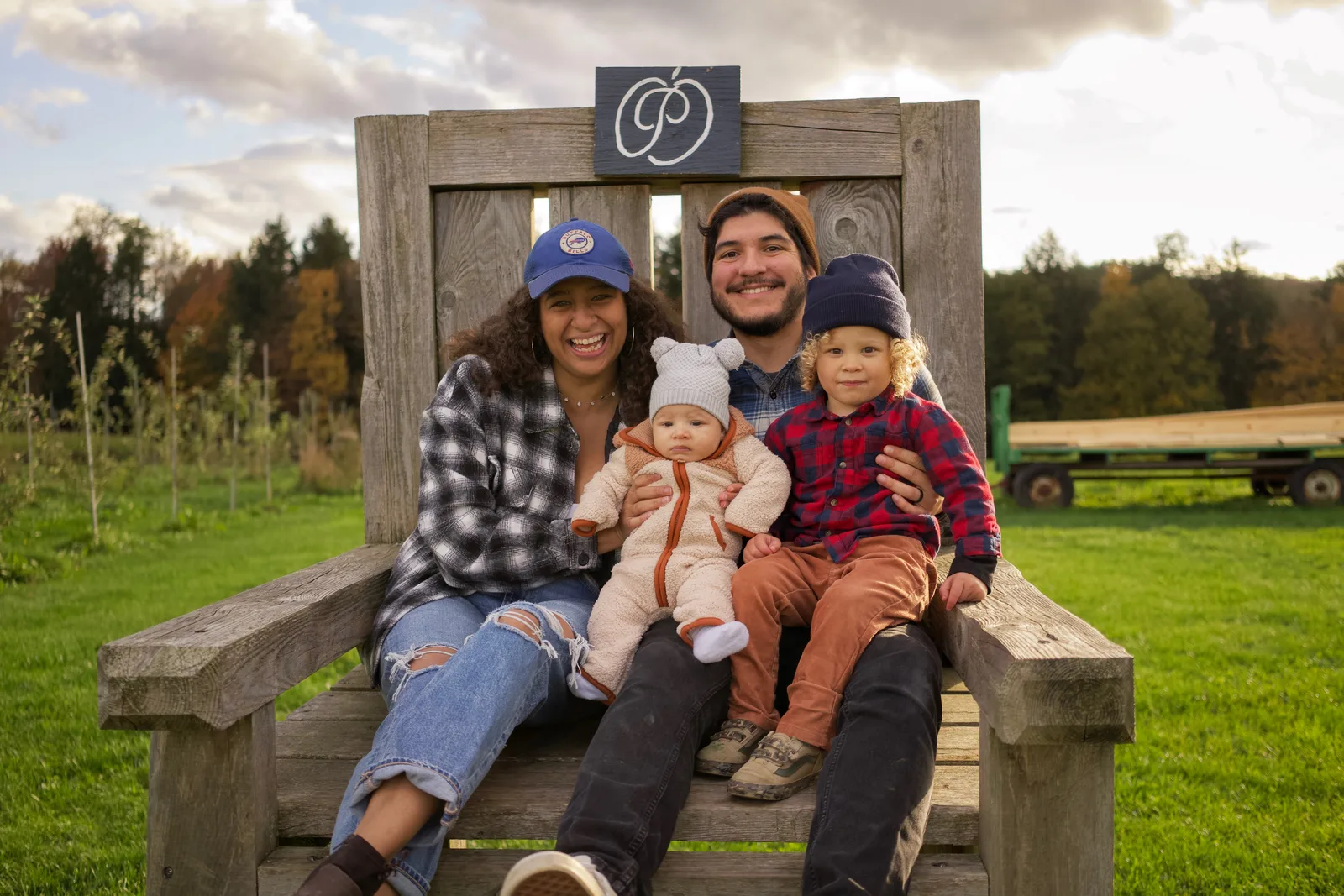 Four people on wooden bench, sign above, orchard rows and golden hour light on landscape
