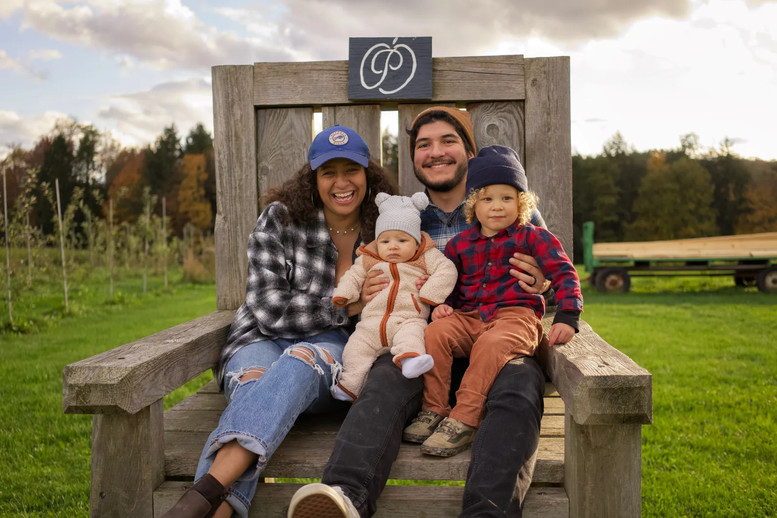 Four people on wooden bench, sign above, grassy field with scattered clouds and hills