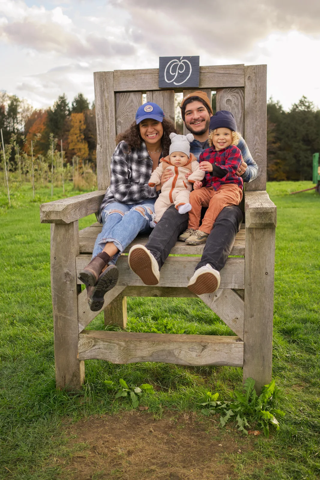 Four people on wooden bench, sign above, open farmland with distant trees and sky