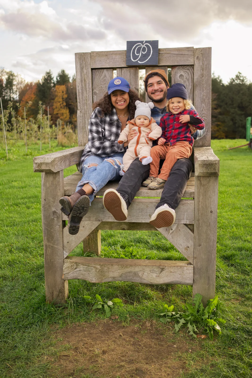 Four people on wooden chair, orchard rows and autumn foliage in background