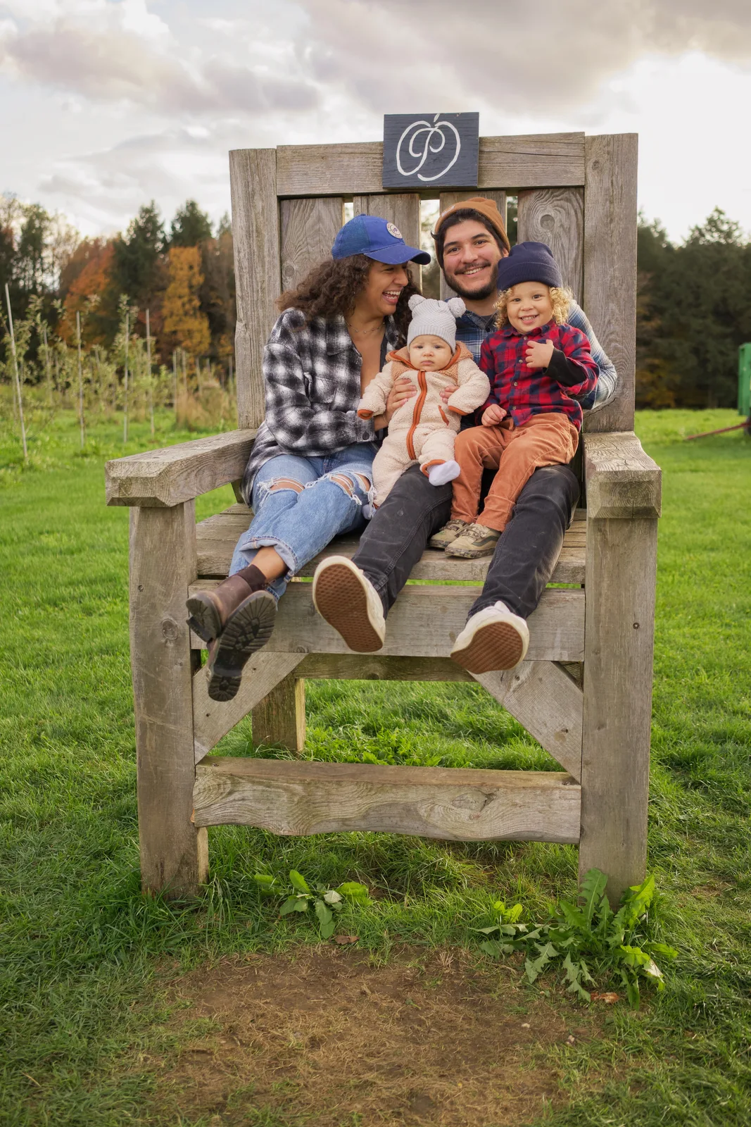 Four people on wooden chair, green grass and cloudy sky over orchard