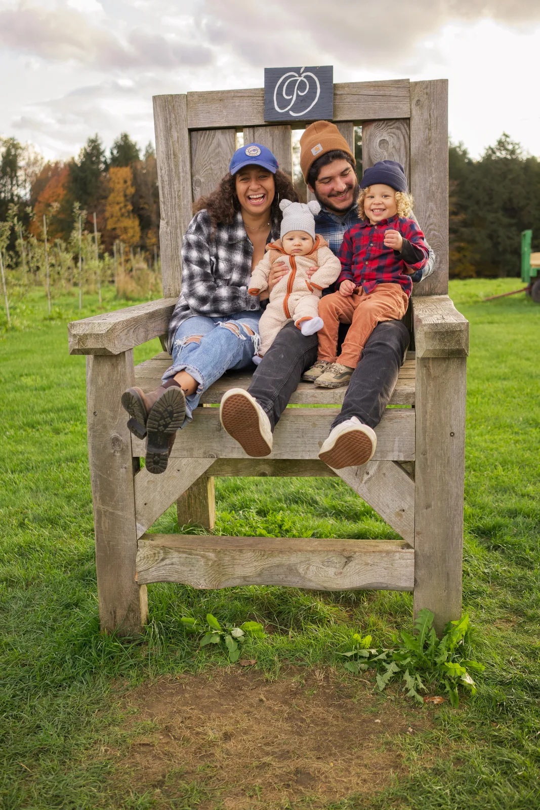 Four people on wooden chair, orchard rows and forested hills in distance