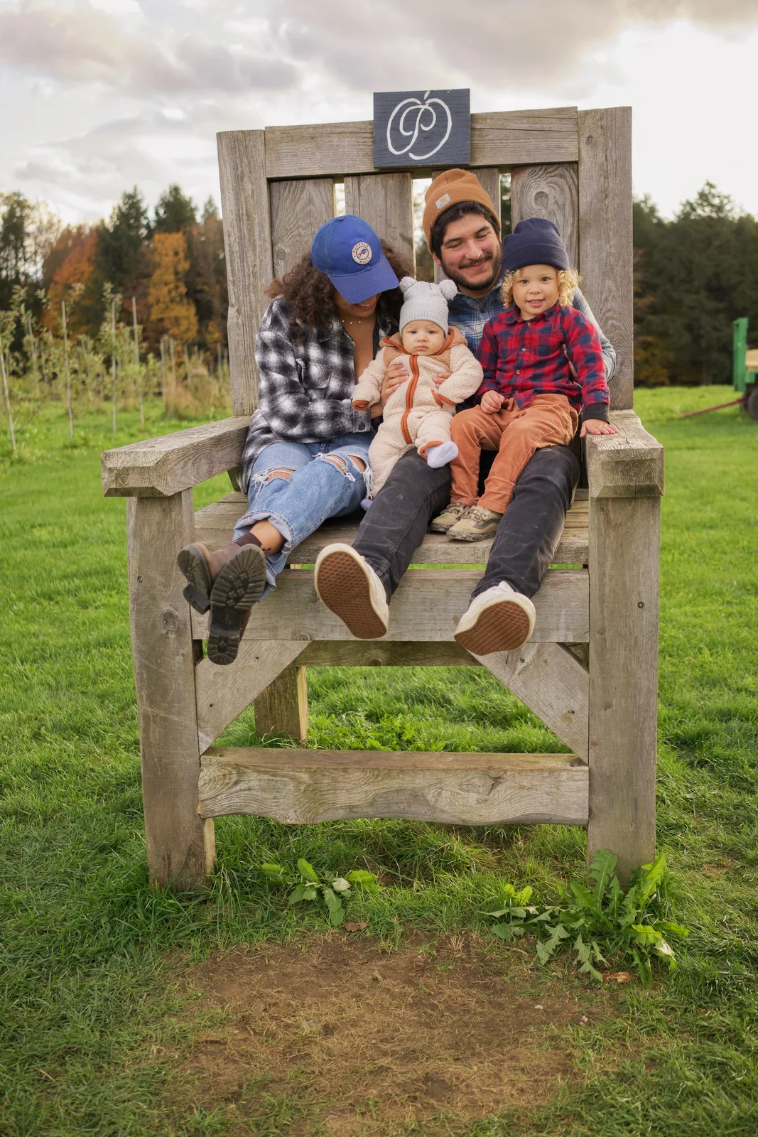 Four people on wooden chair, orchard rows and distant trees under cloudy sky