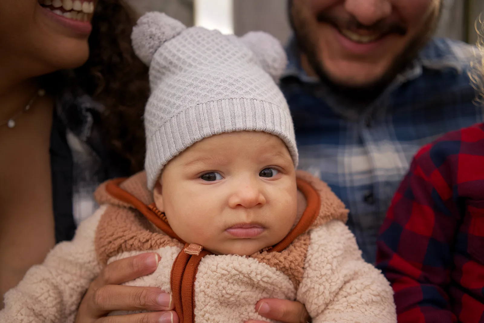 Baby in a light gray knit hat and cream jacket with orange trim held close