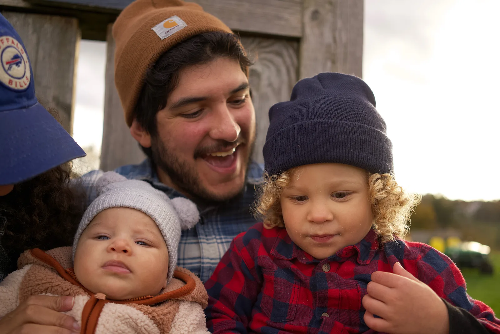 Adult in a blue cap holding a baby in a light gray bear hat and cream jacket