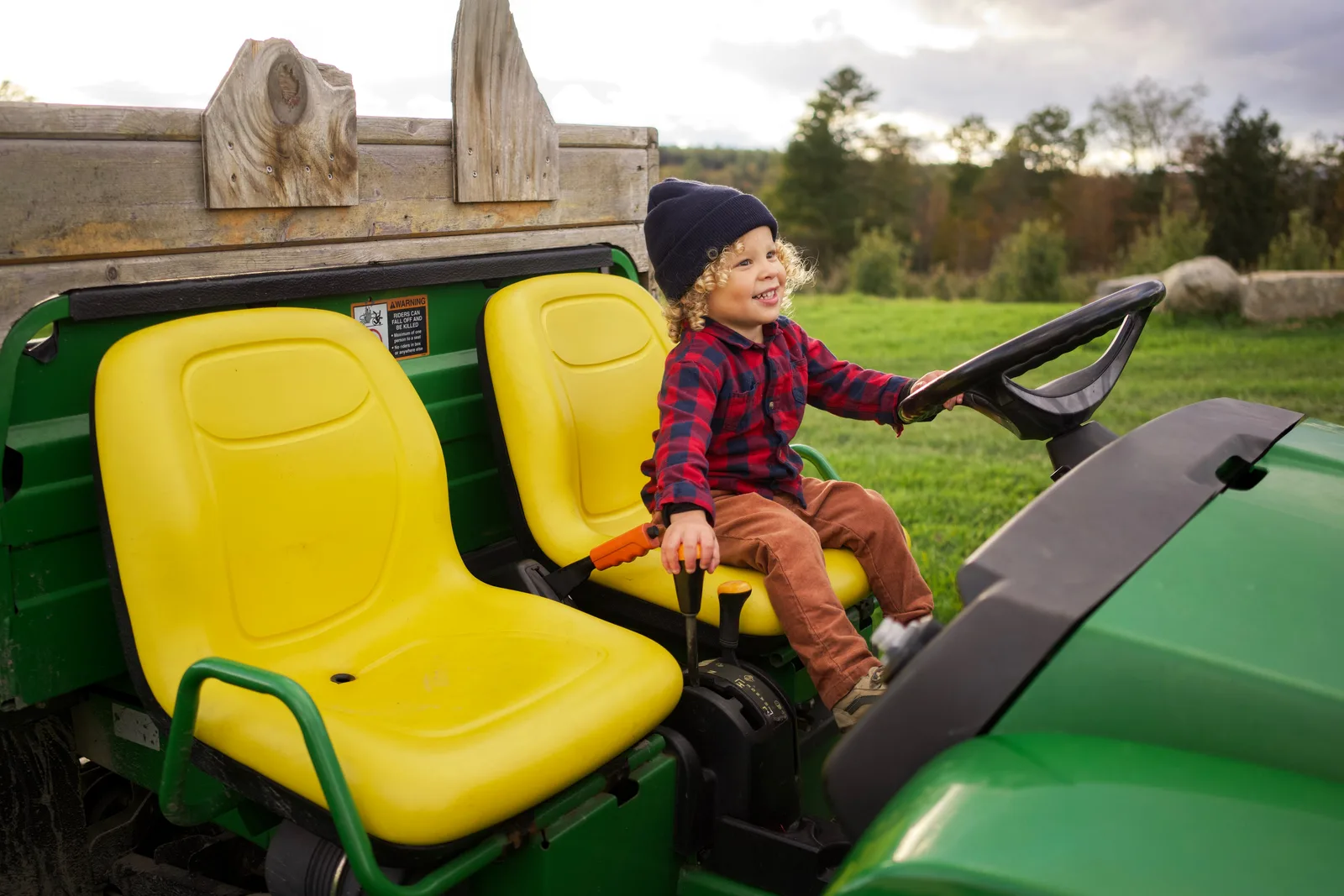 Child in a blue beanie and red plaid shirt sitting on a green tractor