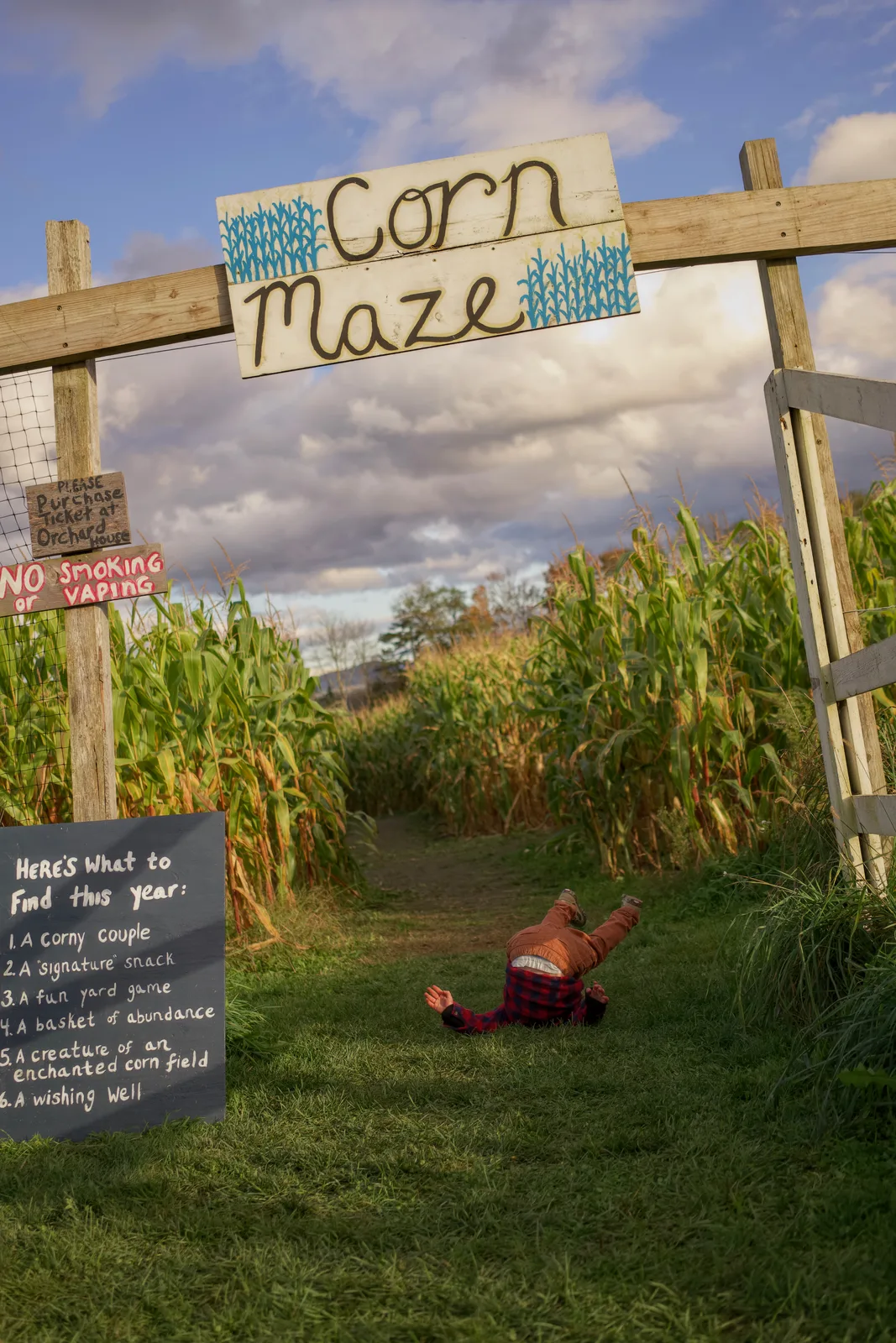 Child in red plaid shirt and blue beanie lying under Corn Maze sign