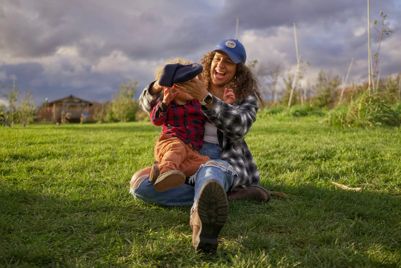 Adult in blue cap and plaid shirt holding child in red plaid shirt on grass