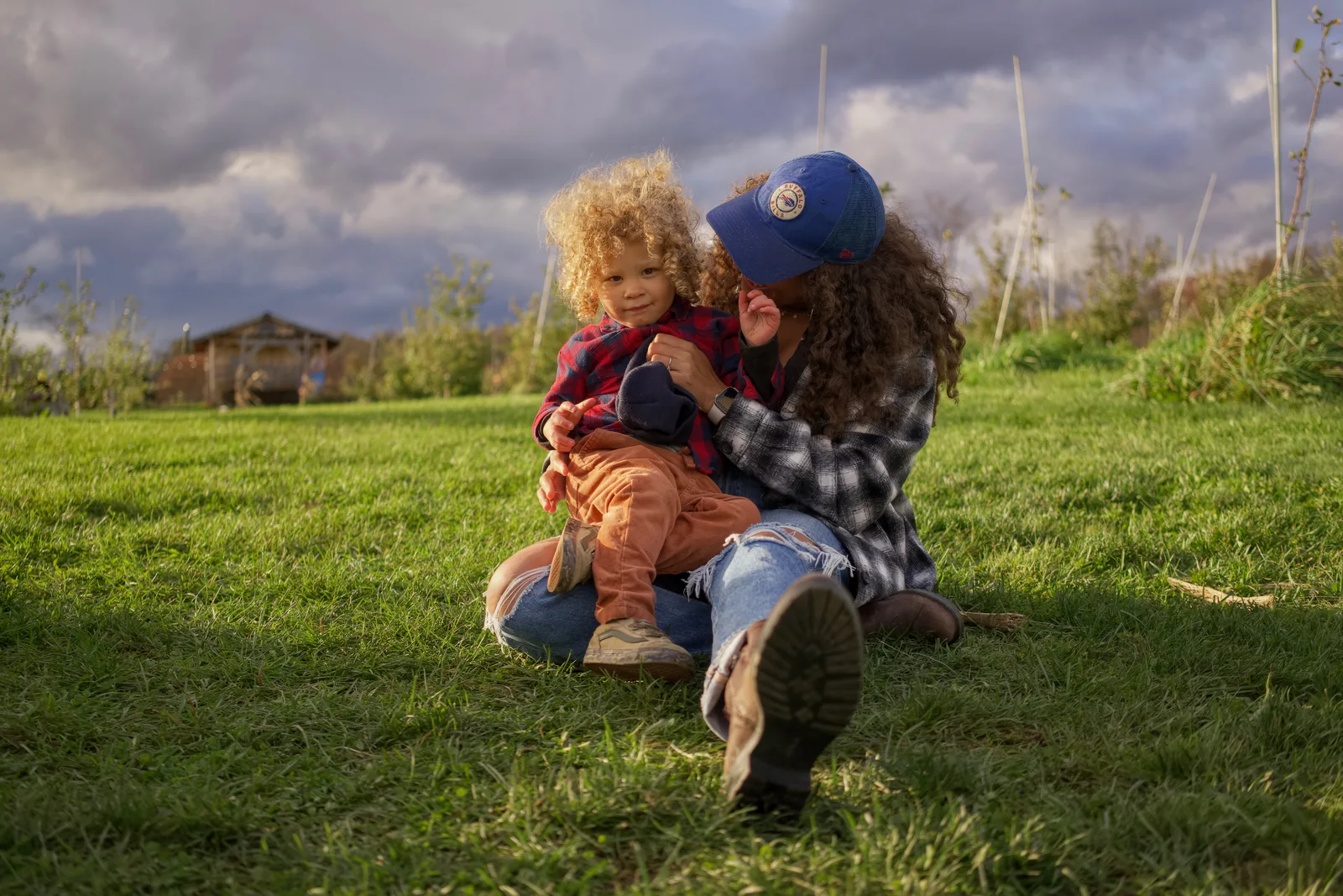 Adult in blue cap and plaid shirt holding child in red plaid shirt on grassy hill