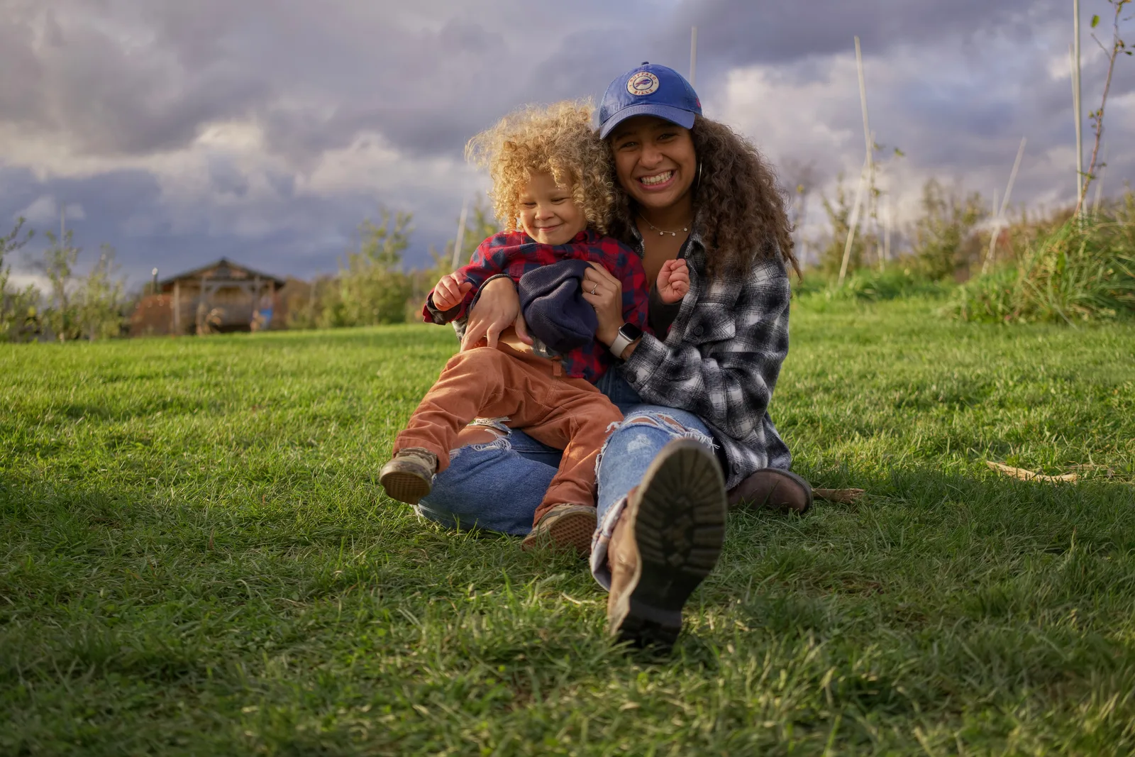 Adult in blue cap and plaid shirt holding child in red plaid shirt on grass