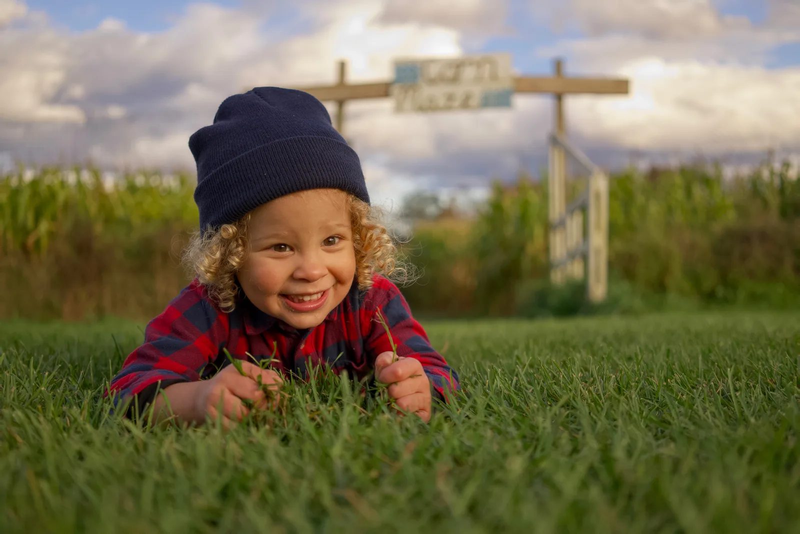 Child in red plaid shirt and dark beanie holding grass on green field