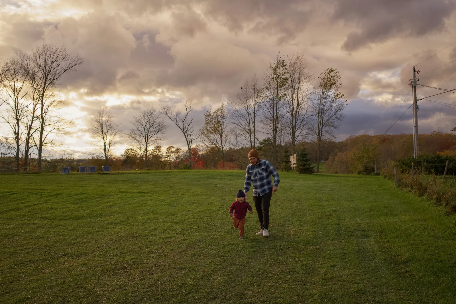 Two people walking on green grass under cloudy sky with trees and utility pole in background