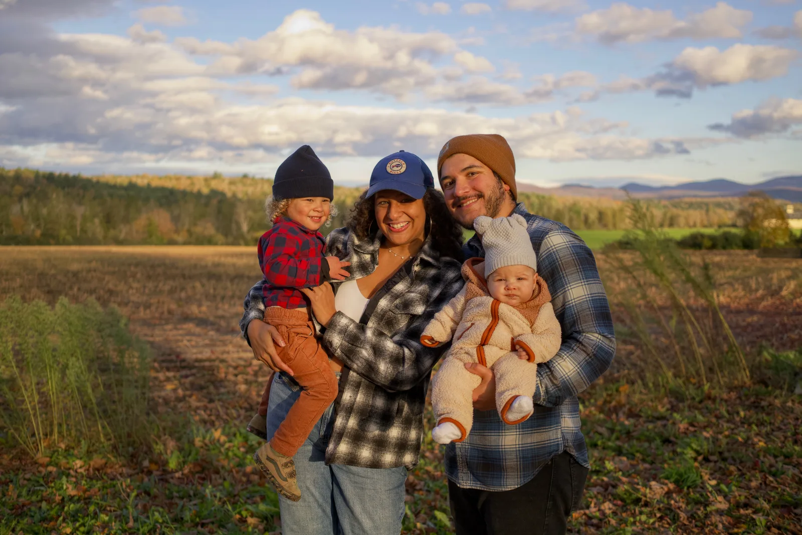 Four people in plaid and beanies holding two children in open field with distant mountains