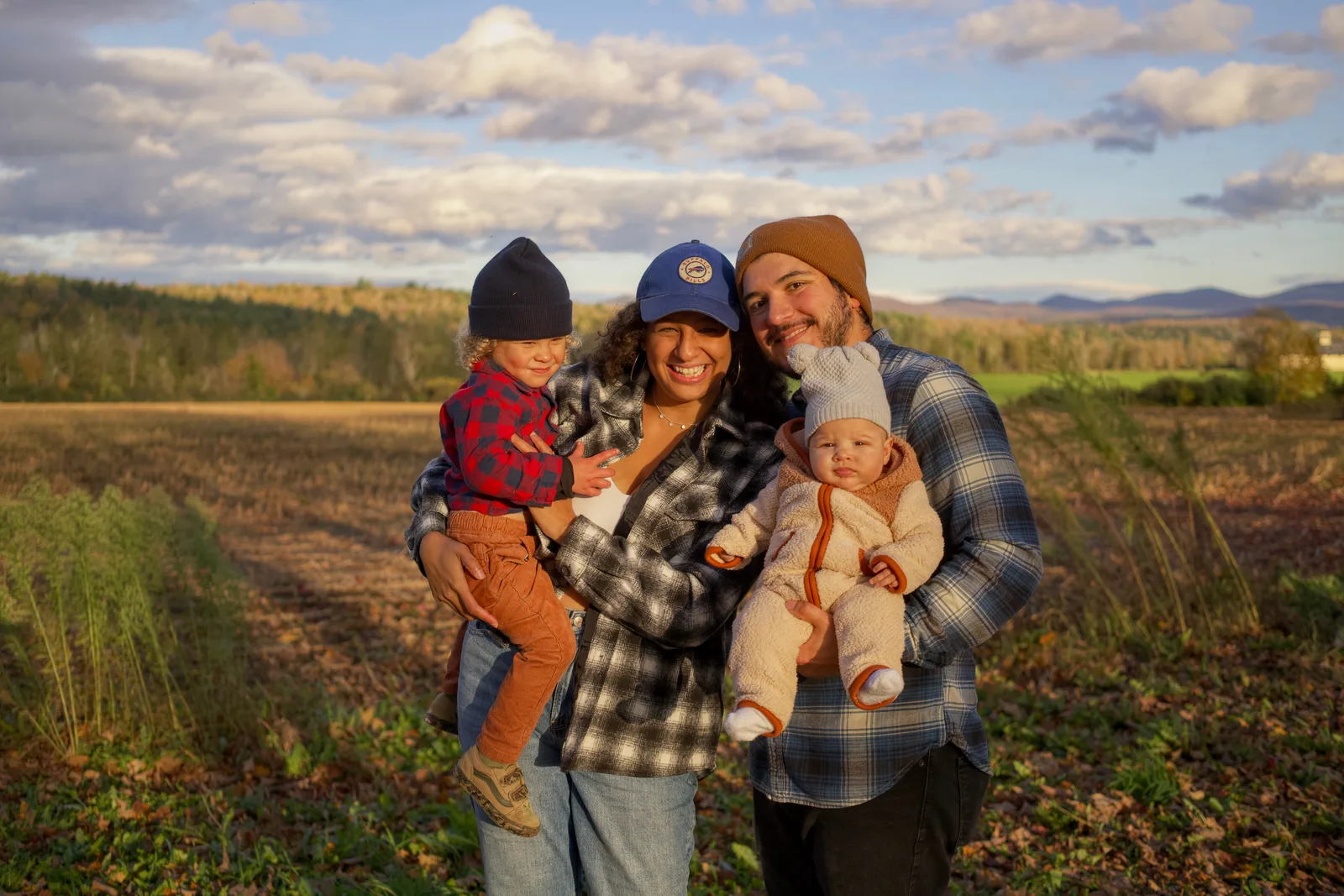 Four people in a field, two adults holding two children, distant trees and mountains