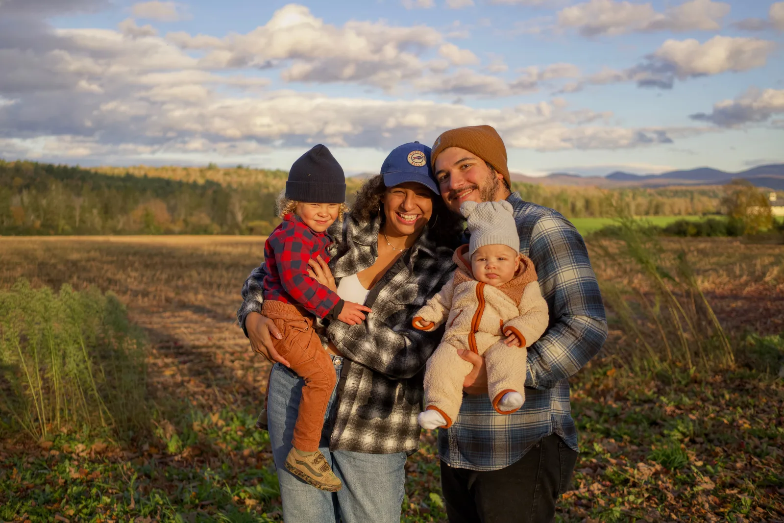 Four people in a field, two adults holding two children, cloudy sky and hills
