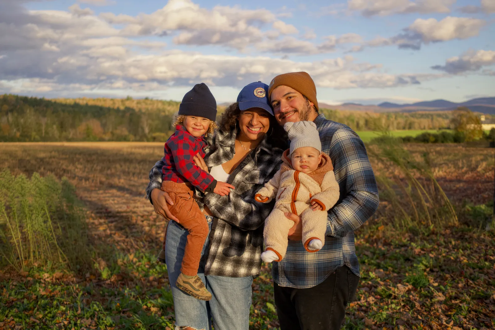 Four people in a field, two adults holding two children, open landscape with mountains