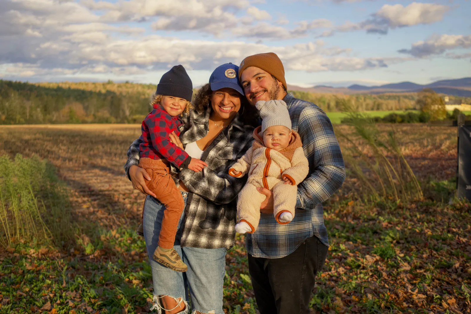 Four people in a field, two adults holding two children, sunset lighting on landscape