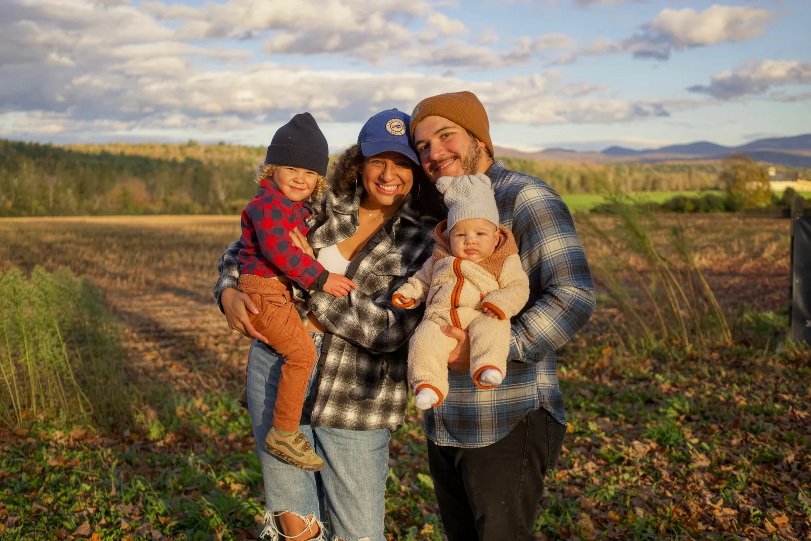 Four people in a field, two adults holding two children, golden hour sky and mountains