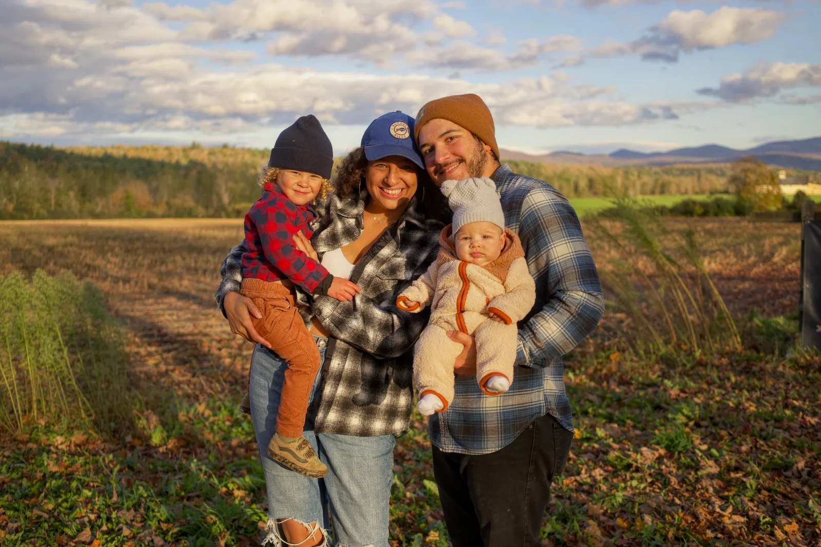 Four people in a field, two adults holding two children, wide open farmland and sky