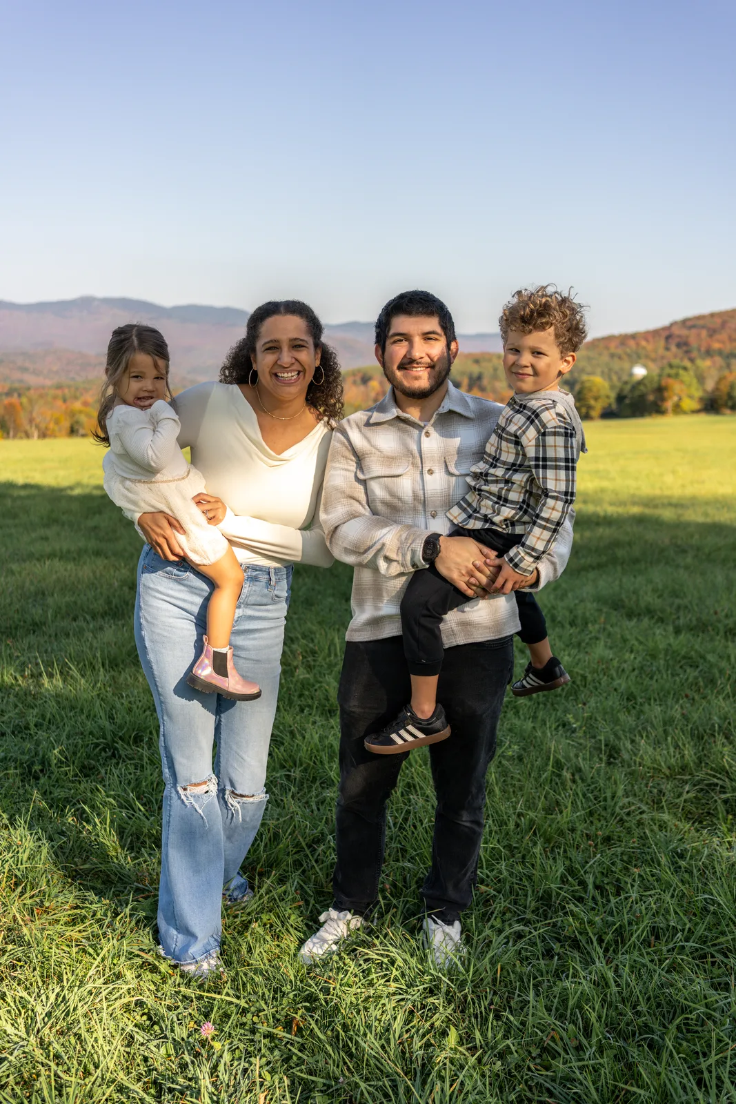 Four people in a grassy field with mountains in the background, two adults holding two children