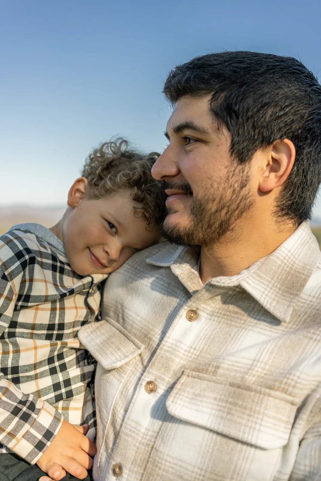 Adult and child with curly hair close together, plaid shirt and light jacket visible