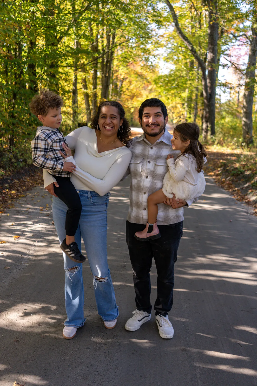 Four people on a wooded road, two adults holding two children in plaid and white