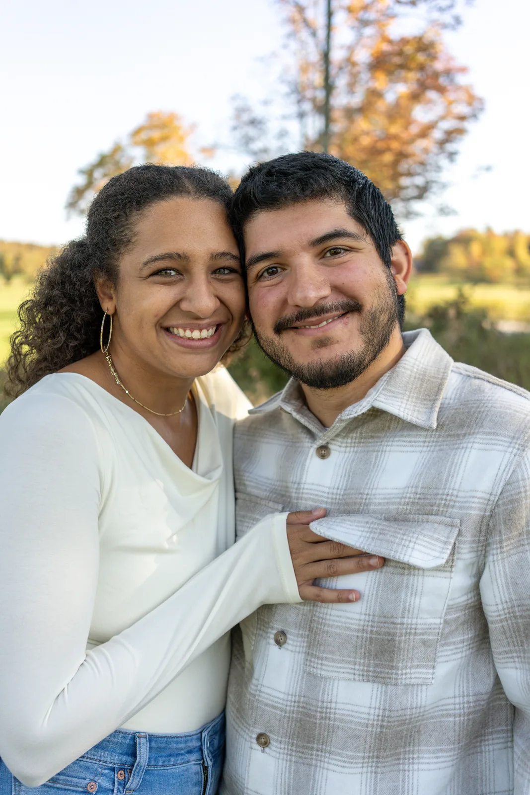 Two adults close together in a field with autumn foliage and distant hills