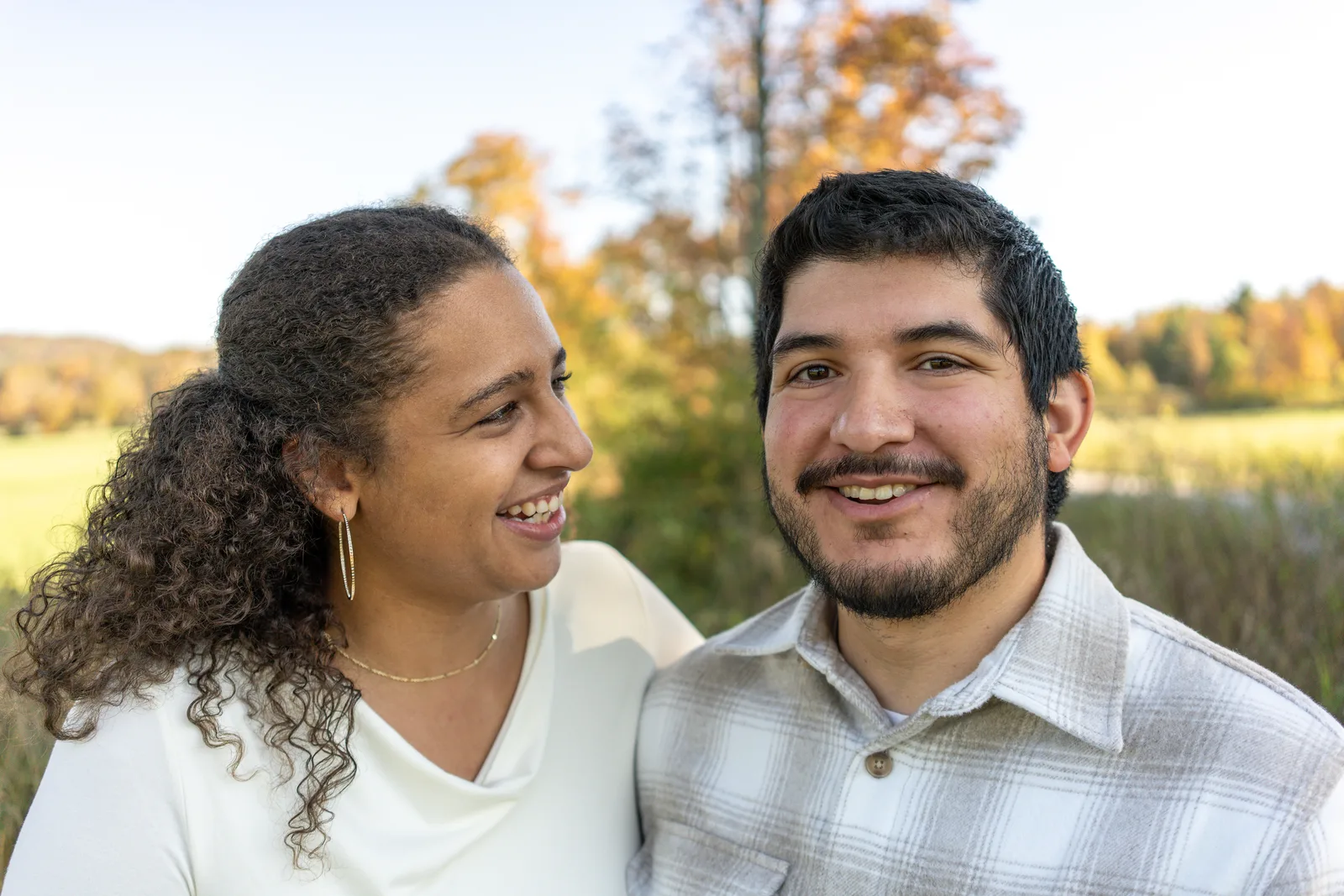 Two adults side by side in a field with autumn trees and distant hills