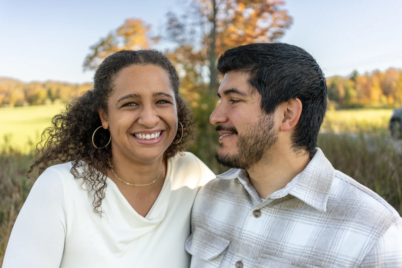 Two adults close together in a field with autumn trees and open sky