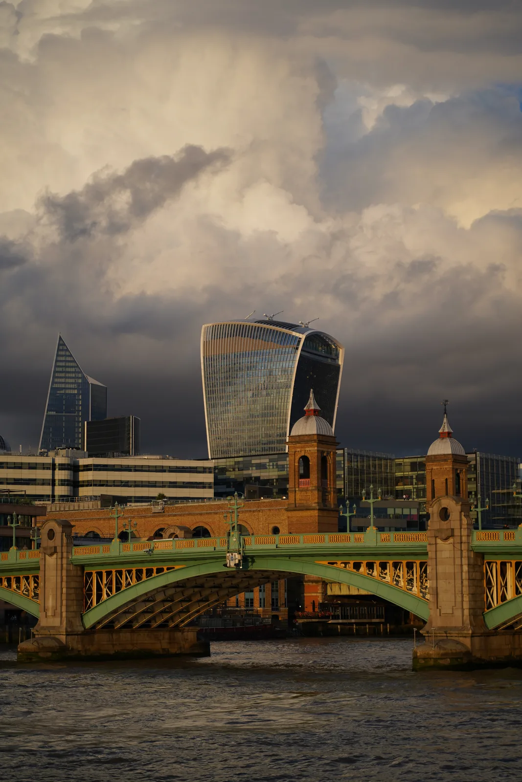 Vertical view of the London skyline, a green bridge, and the River Thames under layered clouds
