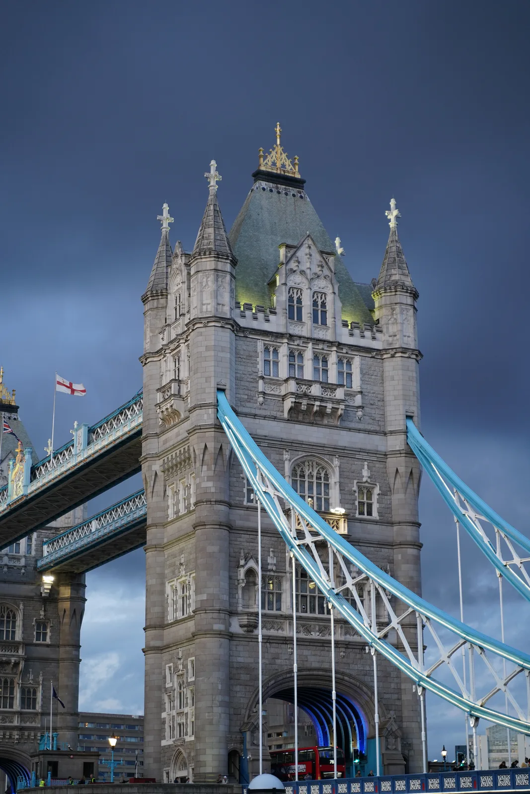 Stone tower and blue suspension cables of Tower Bridge against a dark evening sky
