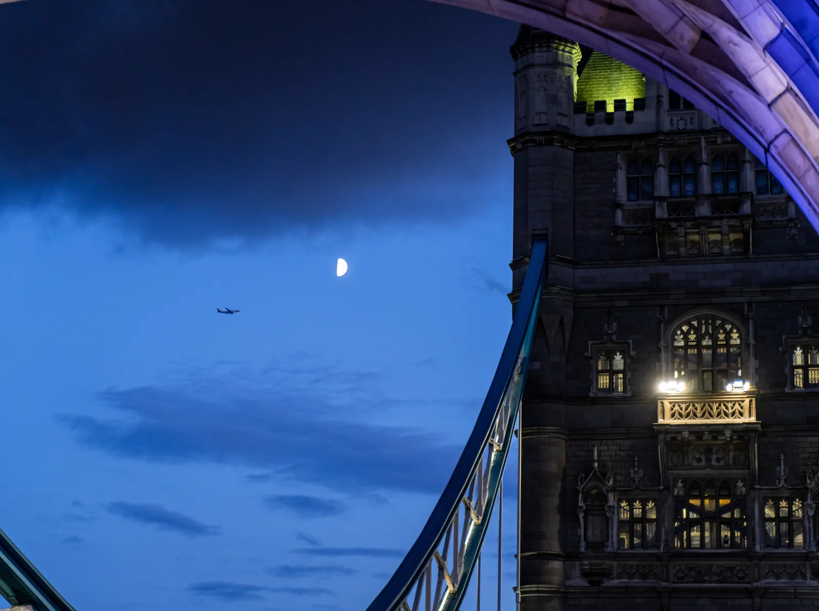 Moon beside one of Tower Bridge's stone towers under a deep blue evening sky