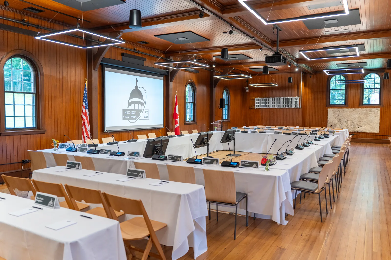 The empty Coach Barn is arranged with a hollow-square conference table, flags, microphones, and place cards.