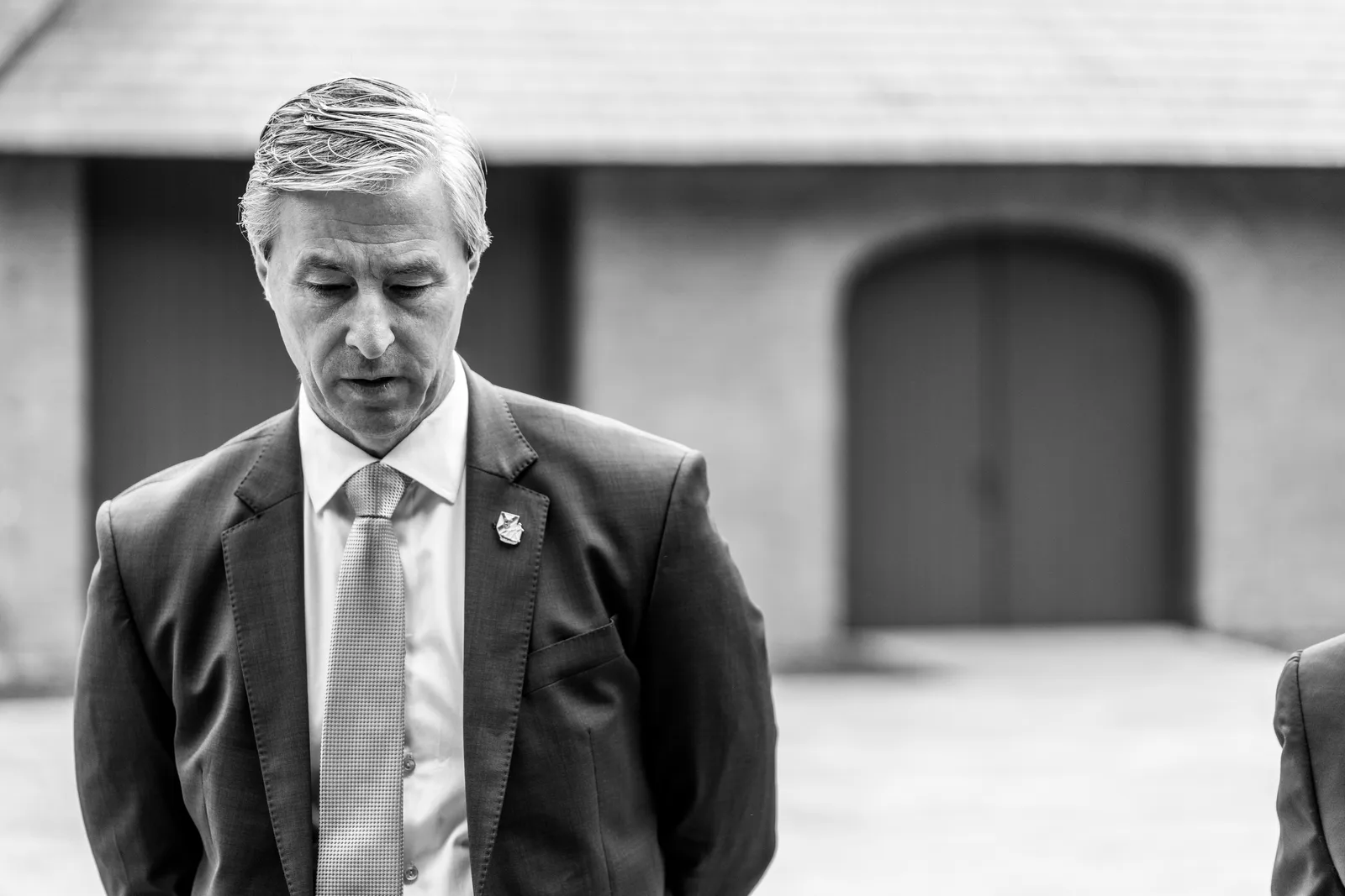 Black-and-white portrait of a suited delegate looking down during an outdoor arrival.