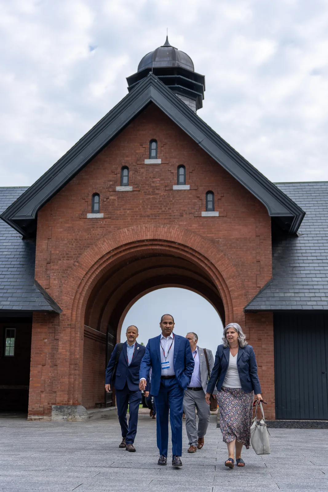 Four delegates walk out of the Coach Barn beneath its tall brick arch.