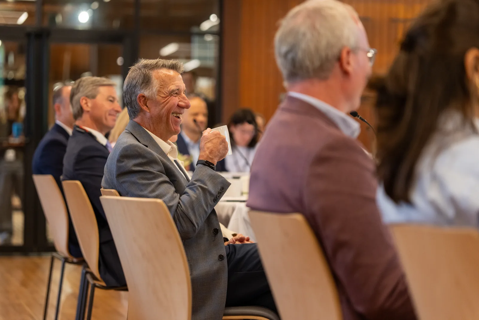 Delegates around the conference table smile as they listen to an opening speaker.