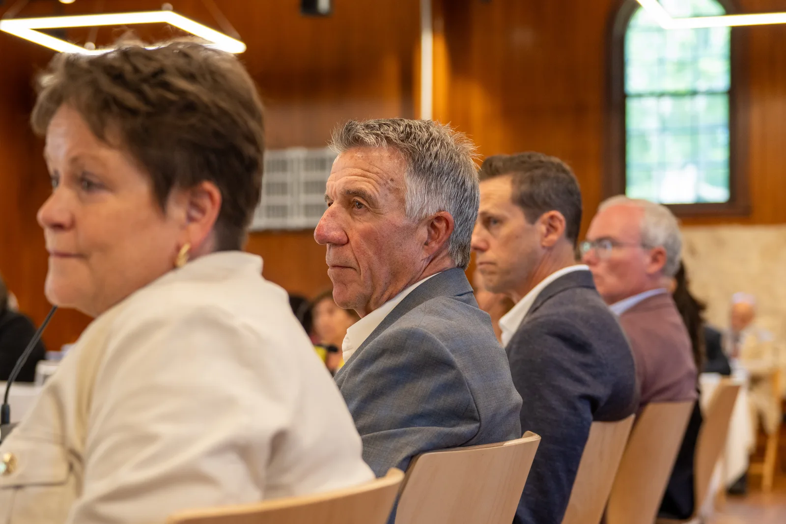 Delegates sit in profile along the table while one participant watches the speaker.