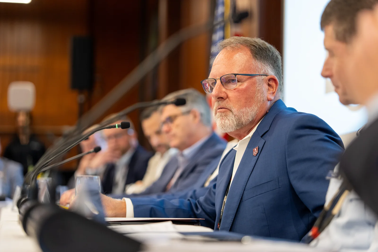 A bearded delegate wearing glasses speaks into a microphone during the working session.
