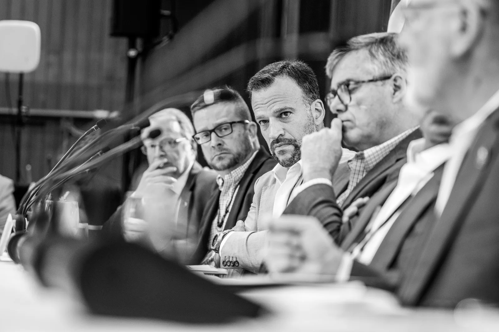 Black-and-white side view of delegates seated shoulder to shoulder behind tabletop microphones.