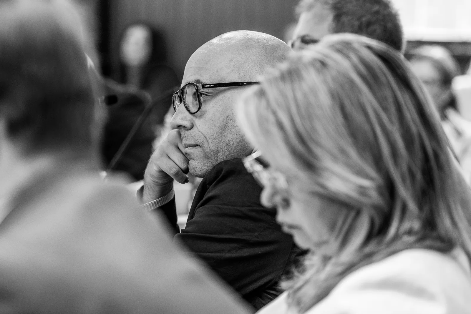 A delegate wearing glasses listens beside a colleague in a black-and-white photograph.