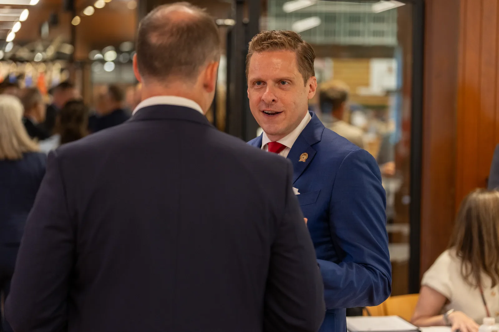 A delegate in a blue suit speaks with a colleague across the conference table.