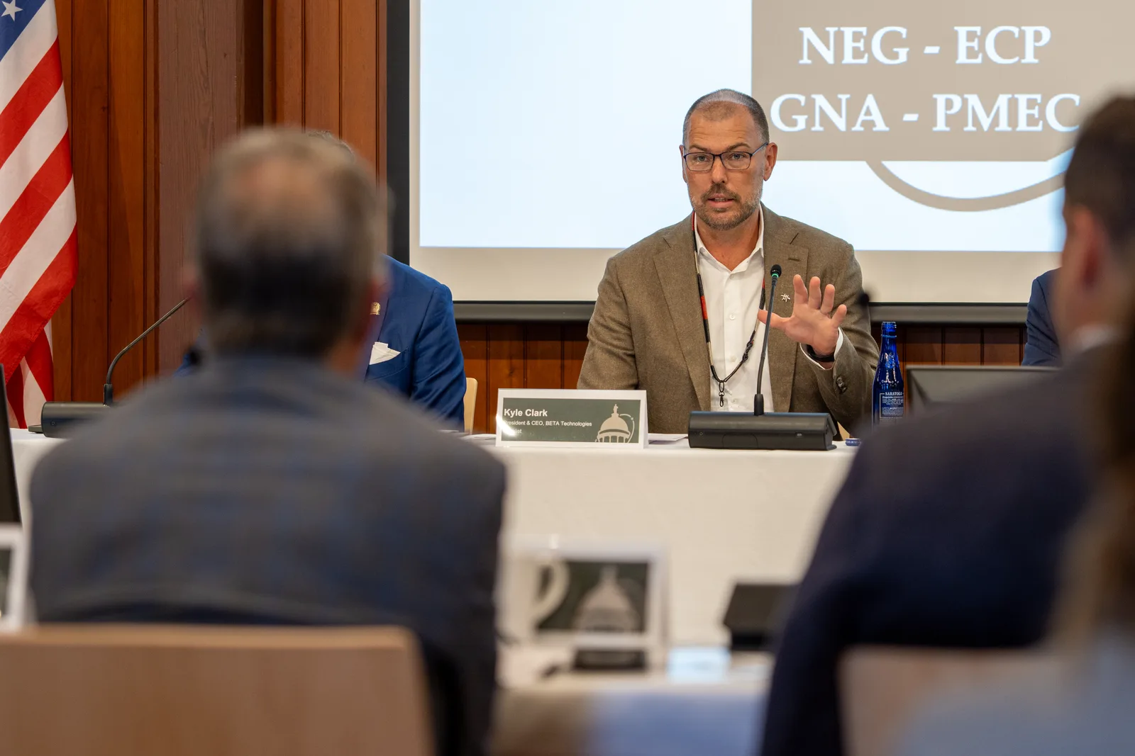 A delegate speaks at the head table beneath the projected NEG-ECP conference mark.