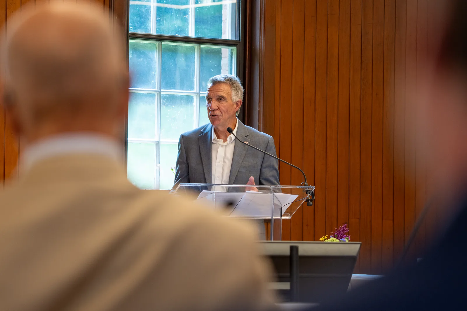 A speaker addresses the conference from a wooden lectern framed by two seated attendees.