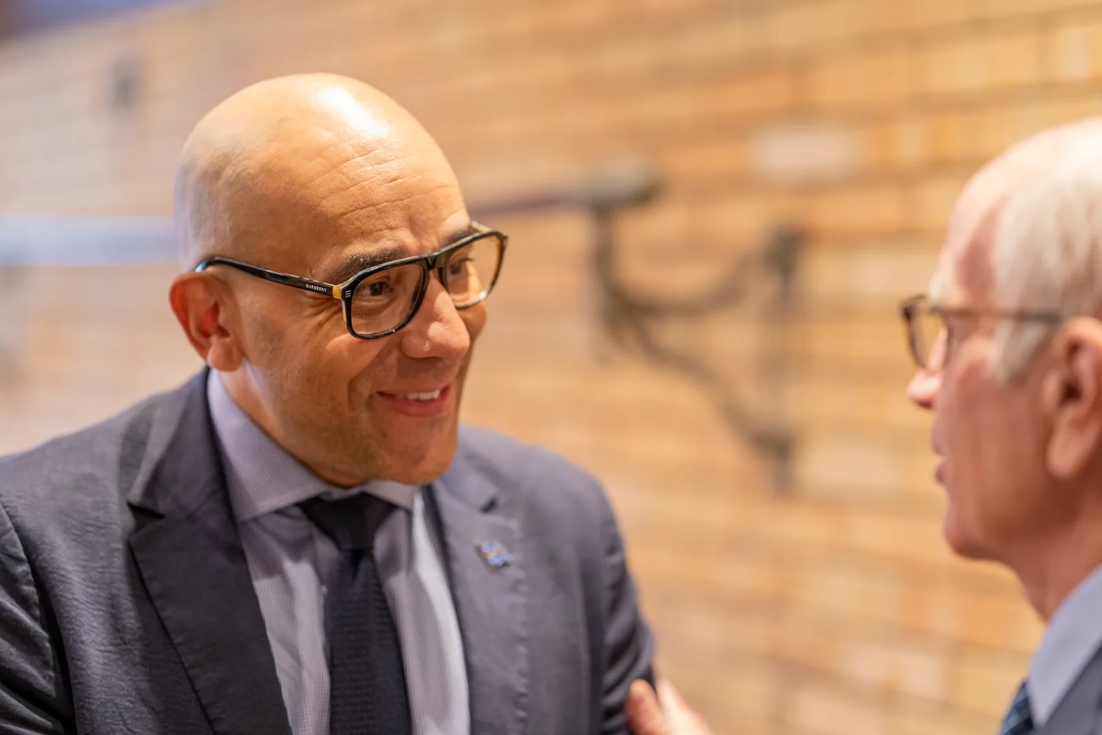 A delegate wearing glasses smiles while speaking with another attendee during a break.