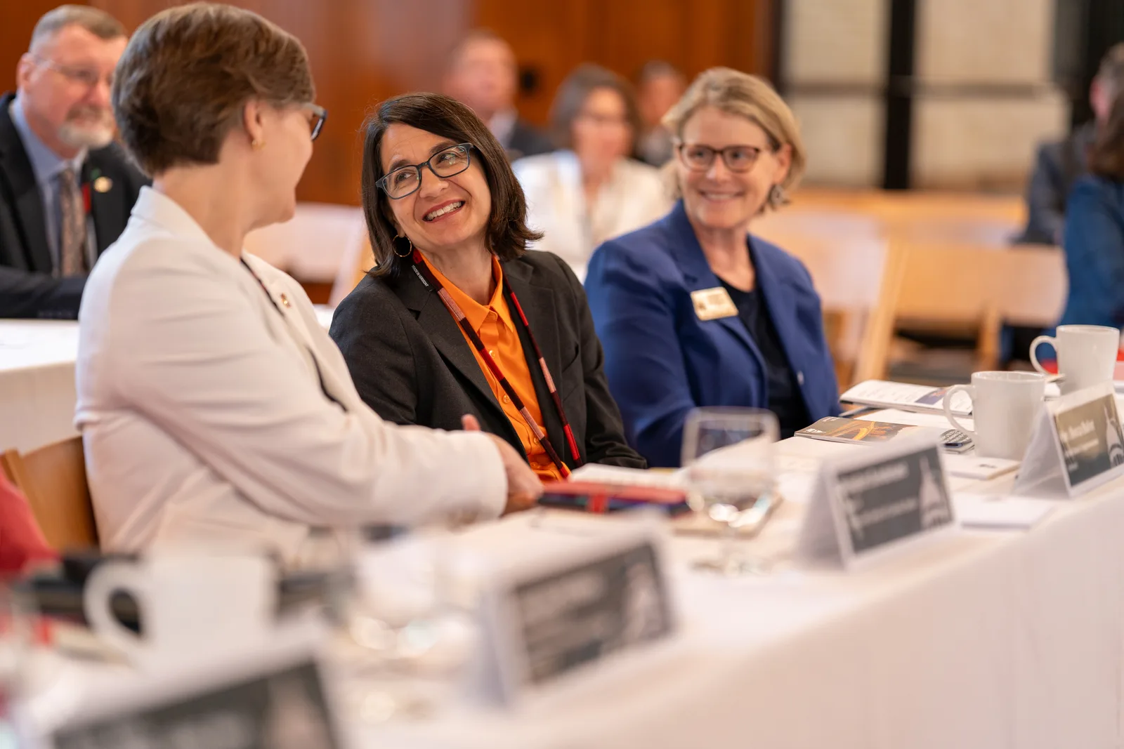 Three women share a laugh across the table during an informal conference exchange.