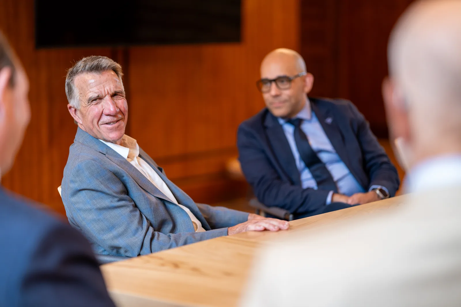 Two delegates sit at the table in conversation as a colleague gestures in the foreground.