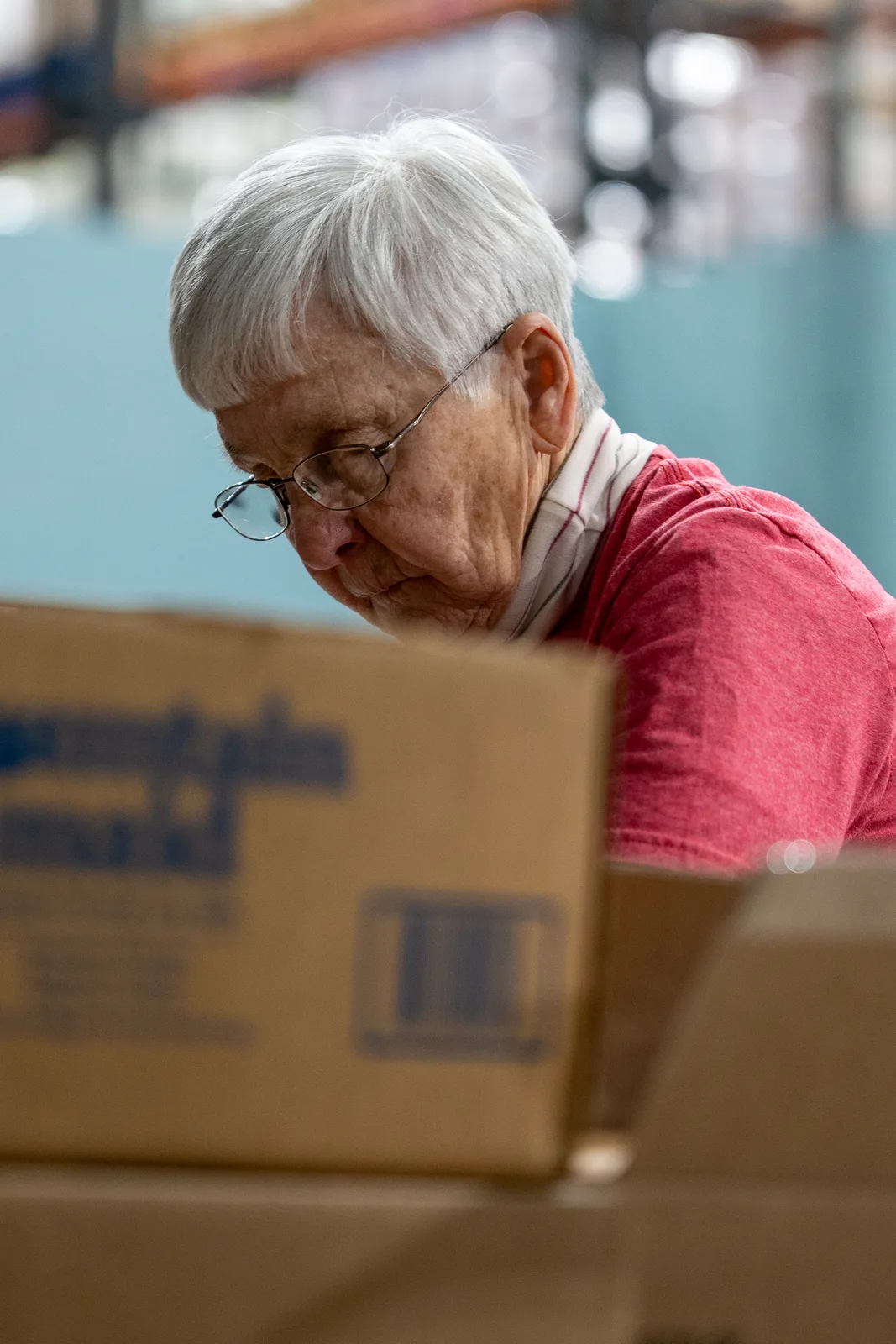 Person in red shirt inspecting a cardboard box in a warehouse with blurred background